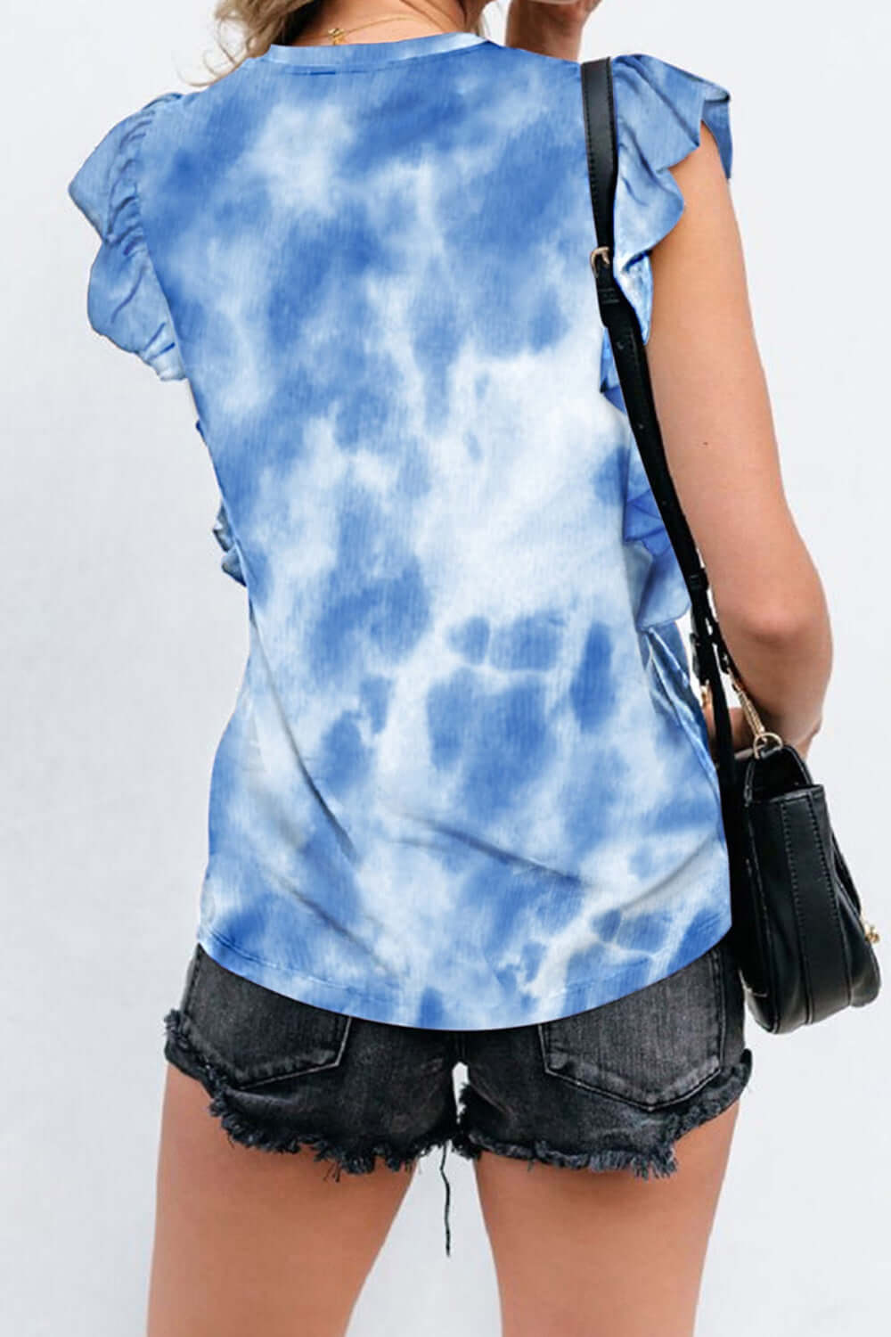 Woman wearing Bella Road Ruffled Printed Round Neck Cap Sleeve T-Shirt in blue pattern, paired with black denim shorts and a black bag.