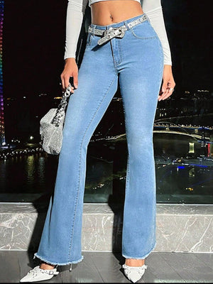 Stylish woman in light wash bootcut jeans with raw hem, accessorized with a sparkling belt and handbag.