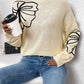 Woman wearing Perfee Mock Neck Dropped Shoulder Long Sleeve Sweater in light yellow with black butterfly design, holding coffee cup