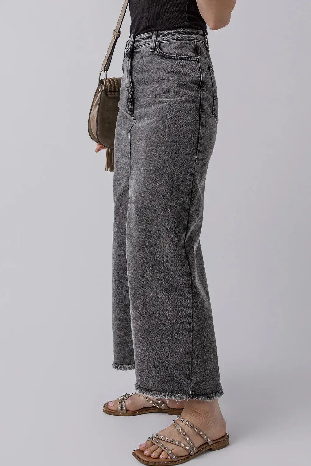 Stylish gray denim skirt with raw hem and pockets, perfect for an edgy look. Model showcasing side view paired with sandals.