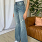 Woman wearing Judy Blue full-size medium rise tummy control destroy flare jeans standing in a living room setting.