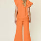 Woman wearing orange texture ruffle short sleeve top and drawstring wide leg pants set, viewed from the back.