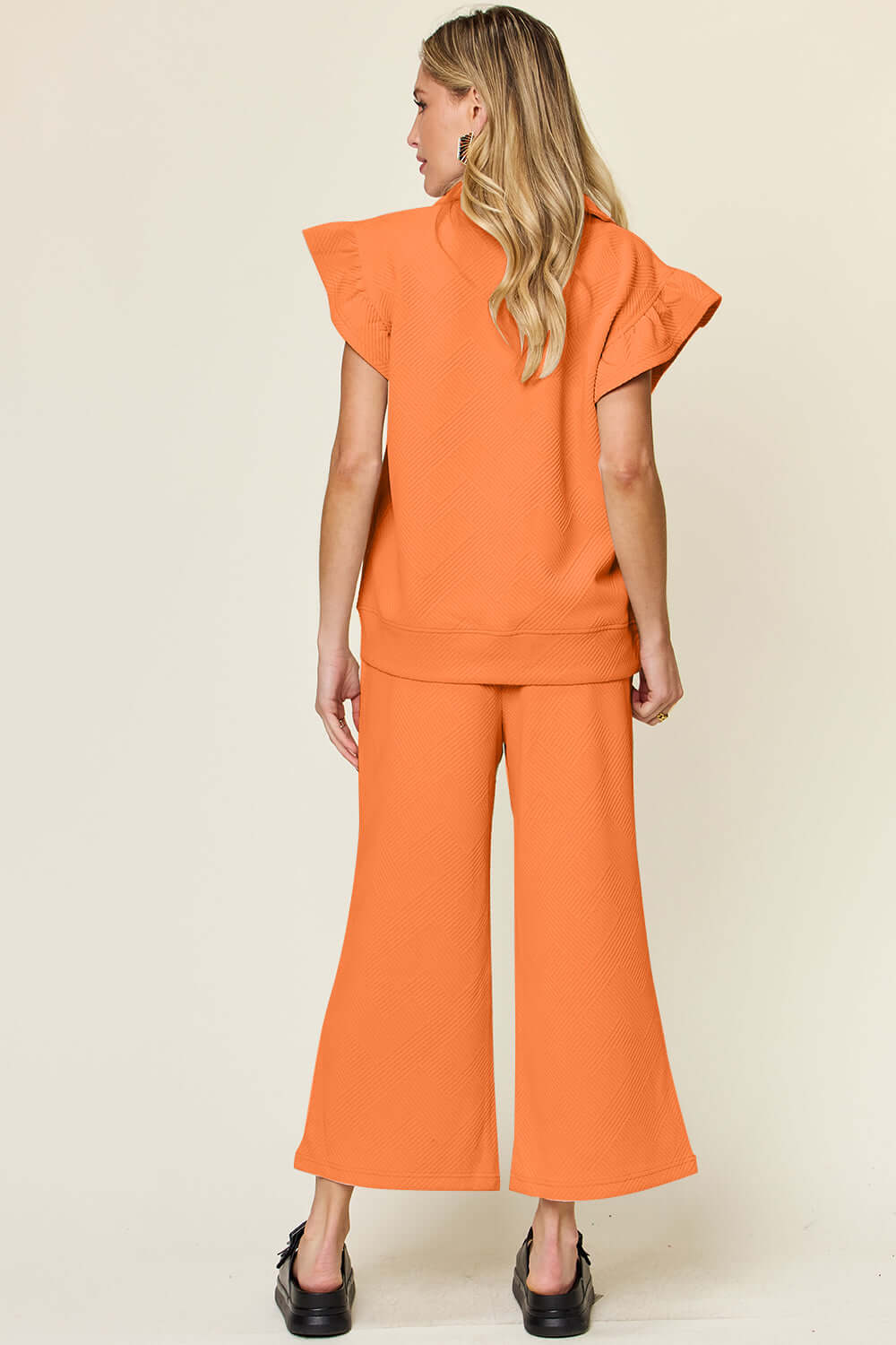 Woman wearing orange texture ruffle short sleeve top and drawstring wide leg pants set, viewed from the back.