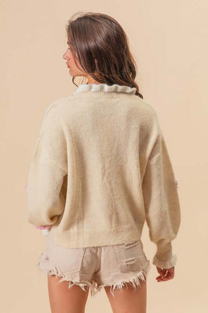 Model showcasing the back of a cream ruffled crochet flower dropped shoulder sweater with casual shorts.