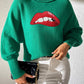 Woman wearing Bella Road Lip Turtleneck Long Sleeve Sweater, green with bold red lips design, styled with white pants.