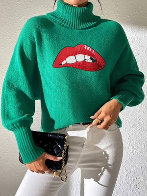 Woman wearing Bella Road Lip Turtleneck Long Sleeve Sweater, green with bold red lips design, styled with white pants.