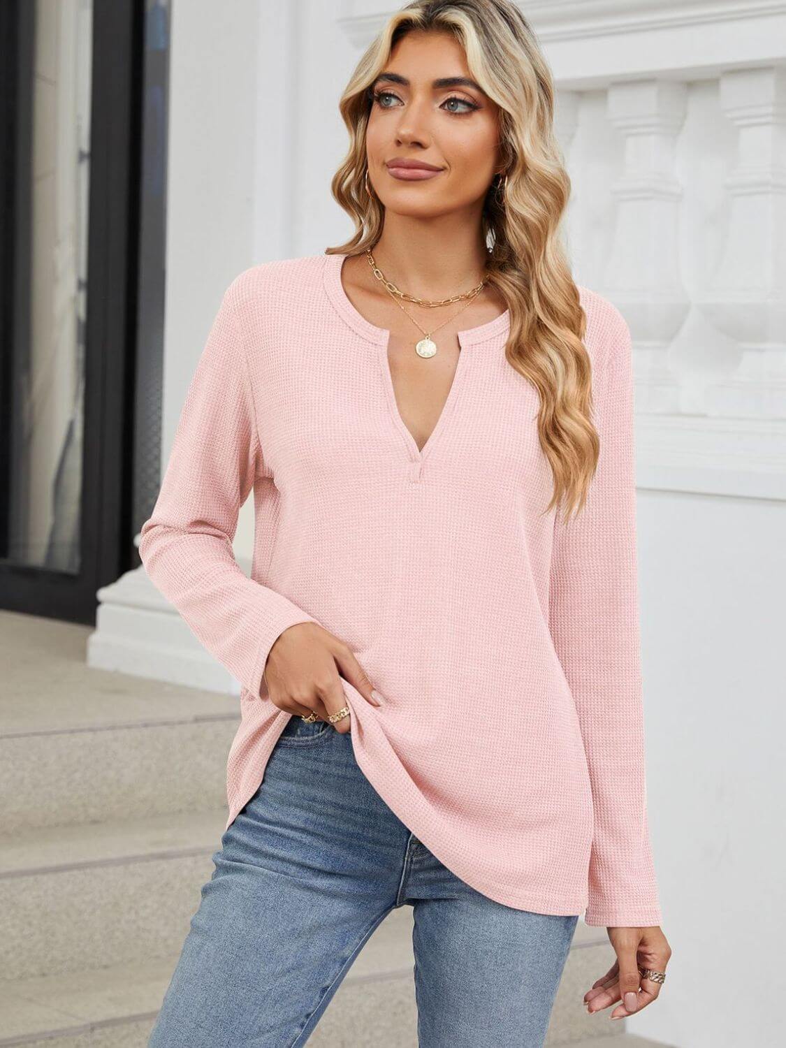 Woman wearing Bella Road Waffle-Knit Notched Long Sleeve T-Shirt in pink paired with blue jeans standing on steps