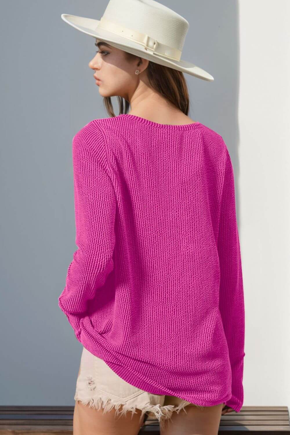 Woman wearing pink notched long sleeve T-shirt with thumbholes and white hat, viewed from the back. Casual and stylish look.