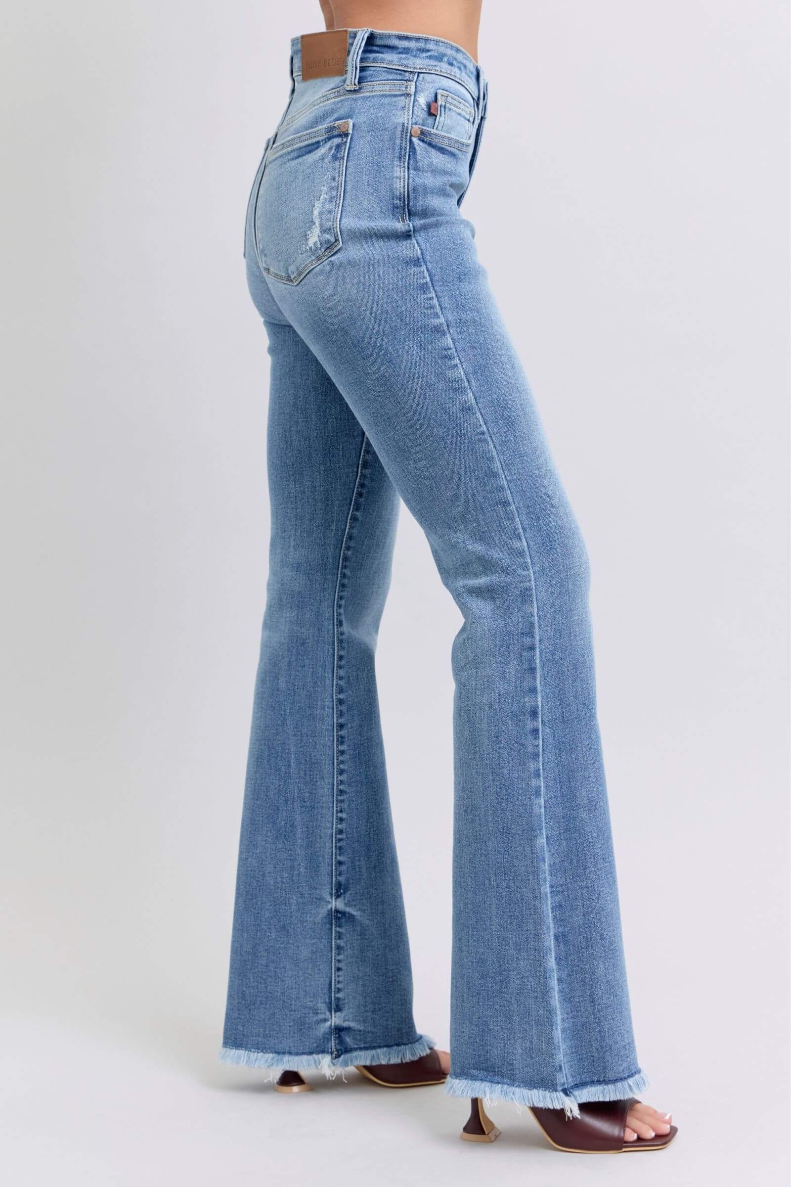 Side view of Judy Blue high rise bootcut jeans with raw hem, showcasing a trendy and flattering silhouette.