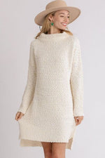 Model in a cozy ivory high-low boucle sweater dress with long sleeves and a chic hat, perfect for colder weather.