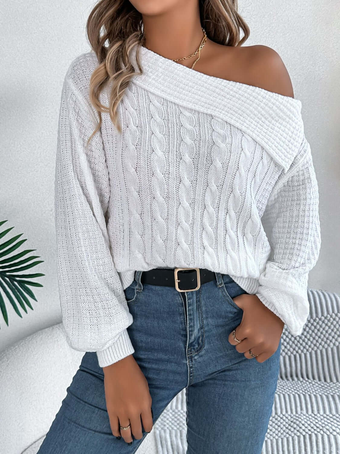 Woman wearing Bella Road Cable-Knit One Shoulder Long Sleeve Sweater in white, paired with blue jeans and a black belt.