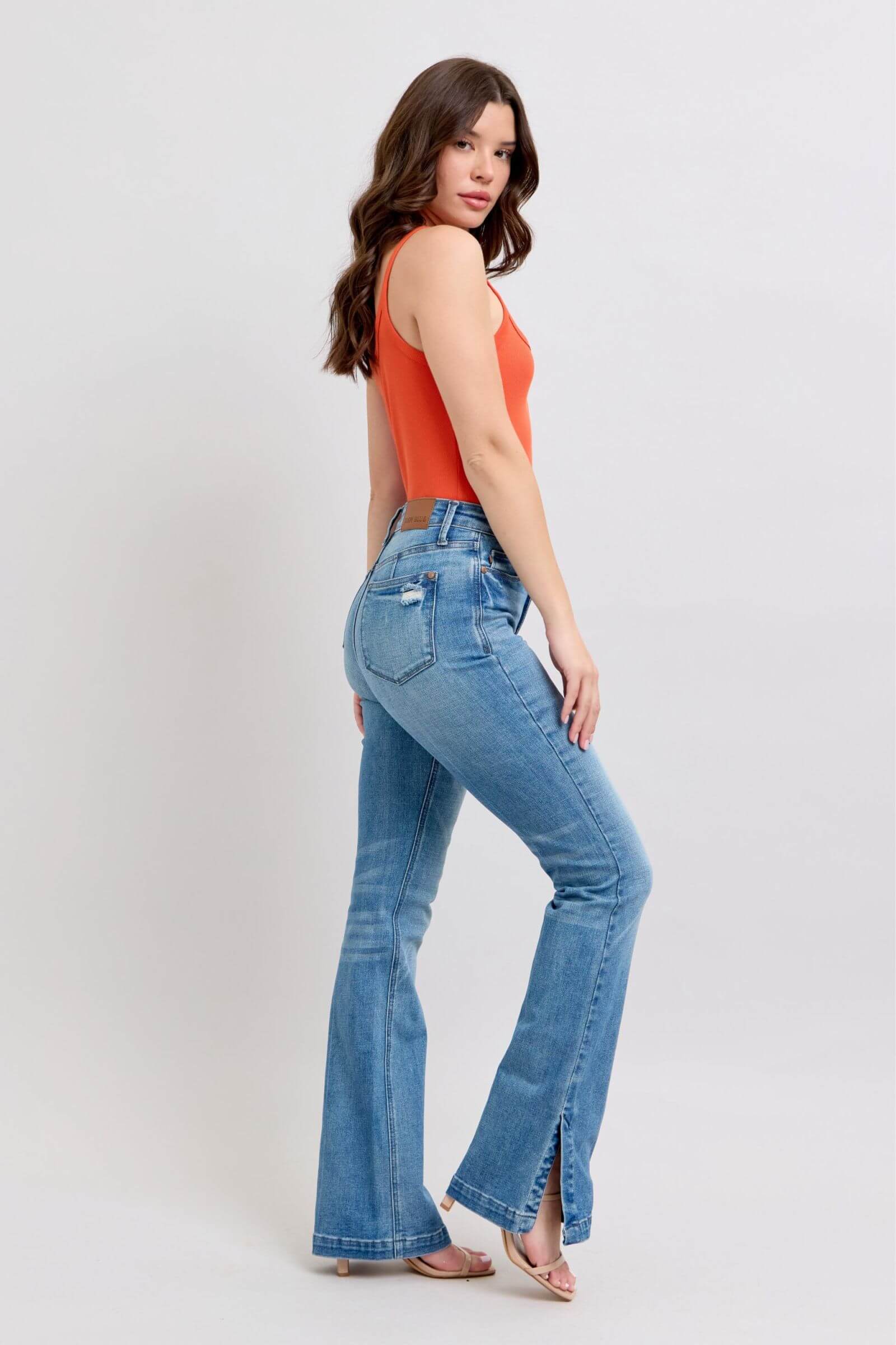 Model wearing high waist tummy control vintage wash slim boot jeans with side slits and an orange top.