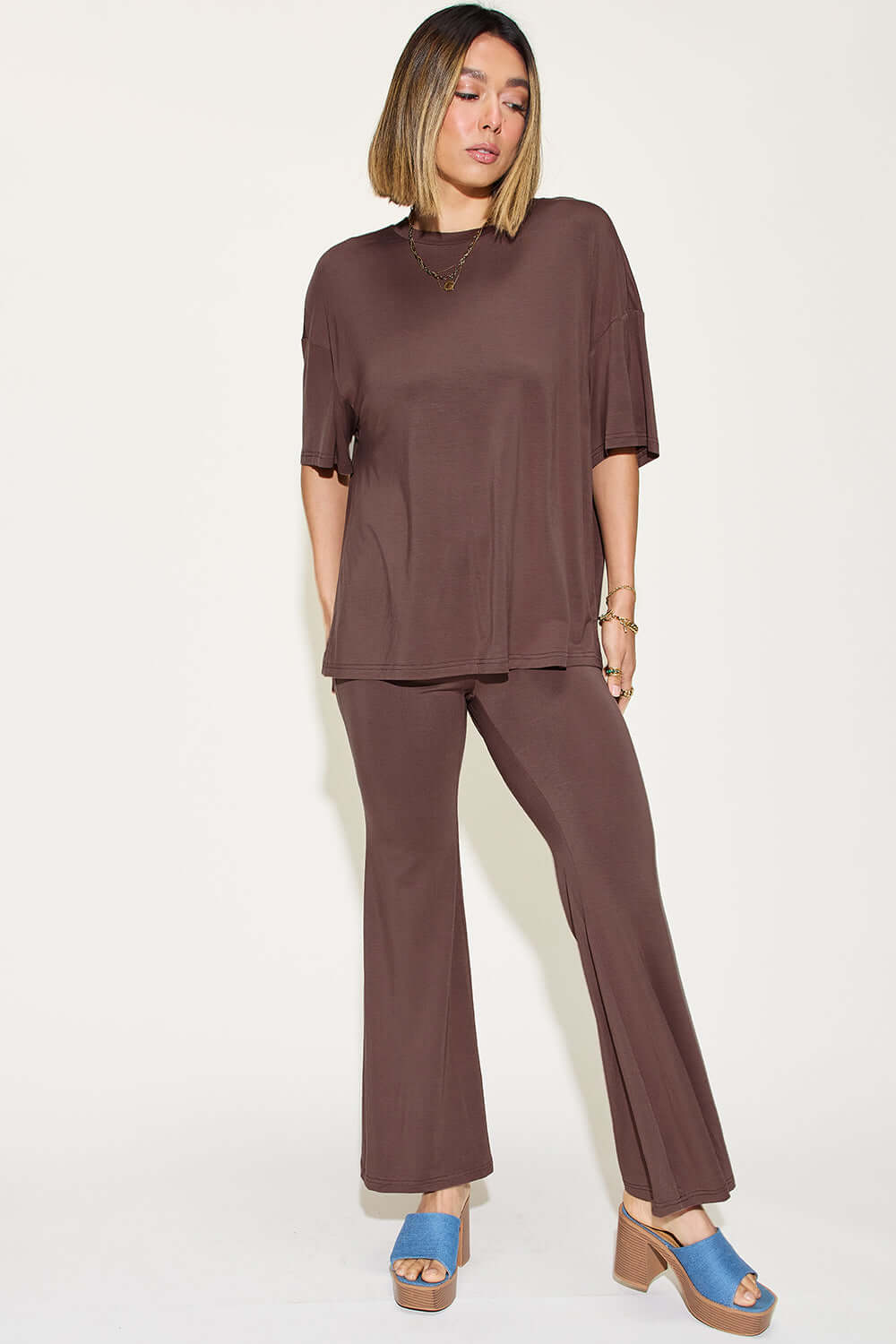 Woman wearing a bamboo drop shoulder t-shirt and flare pants set in brown, featuring a relaxed fit and paired with blue platform sandals.