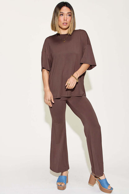 Woman wearing bamboo drop shoulder T-shirt and flare pants set in brown, standing in a casual pose with blue heeled sandals.