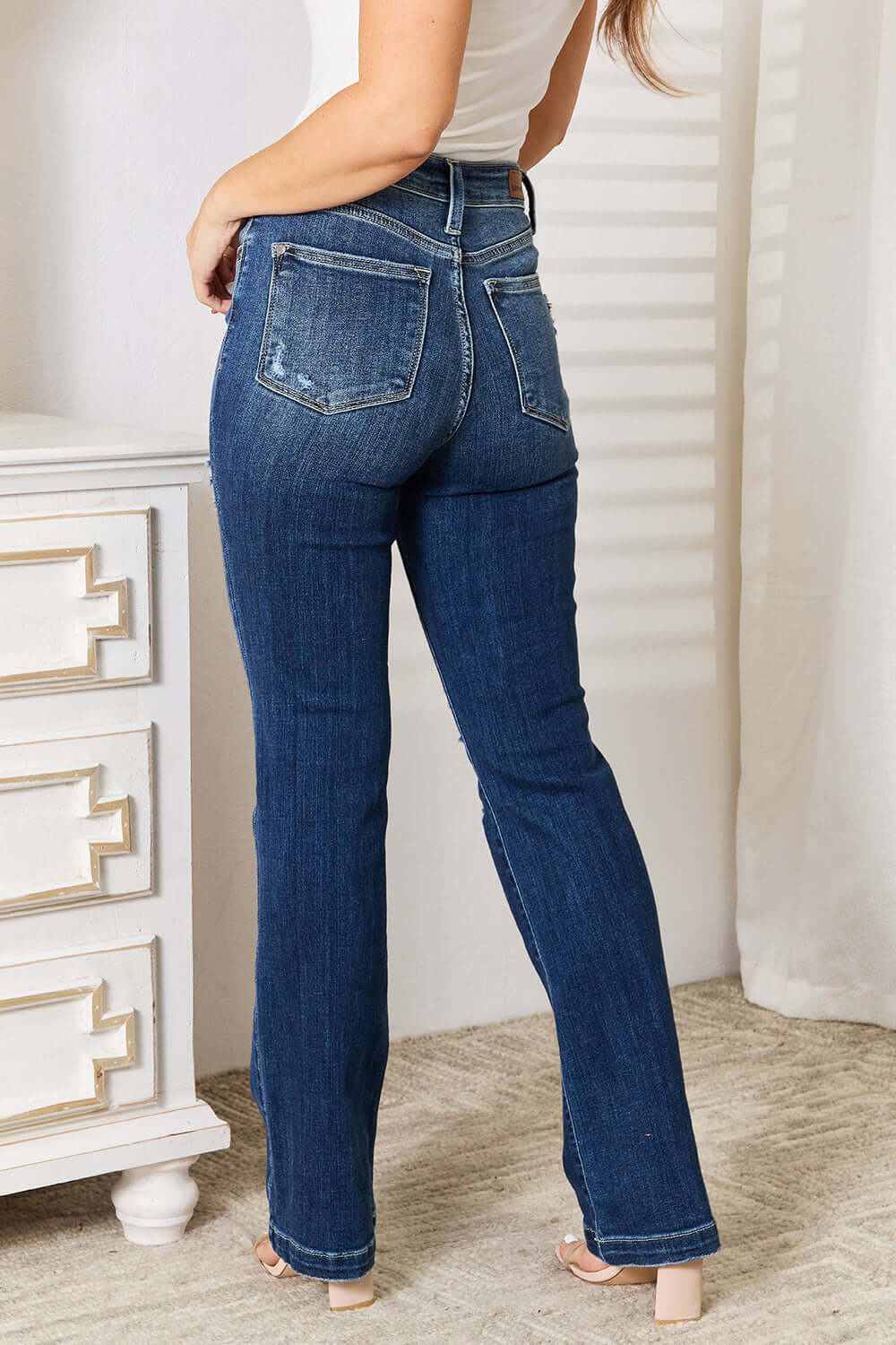 Back view of woman wearing Judy Blue Mid Rise Hand Sand & Destroy Bootcut Jeans Petite, showcasing fit and distressed details