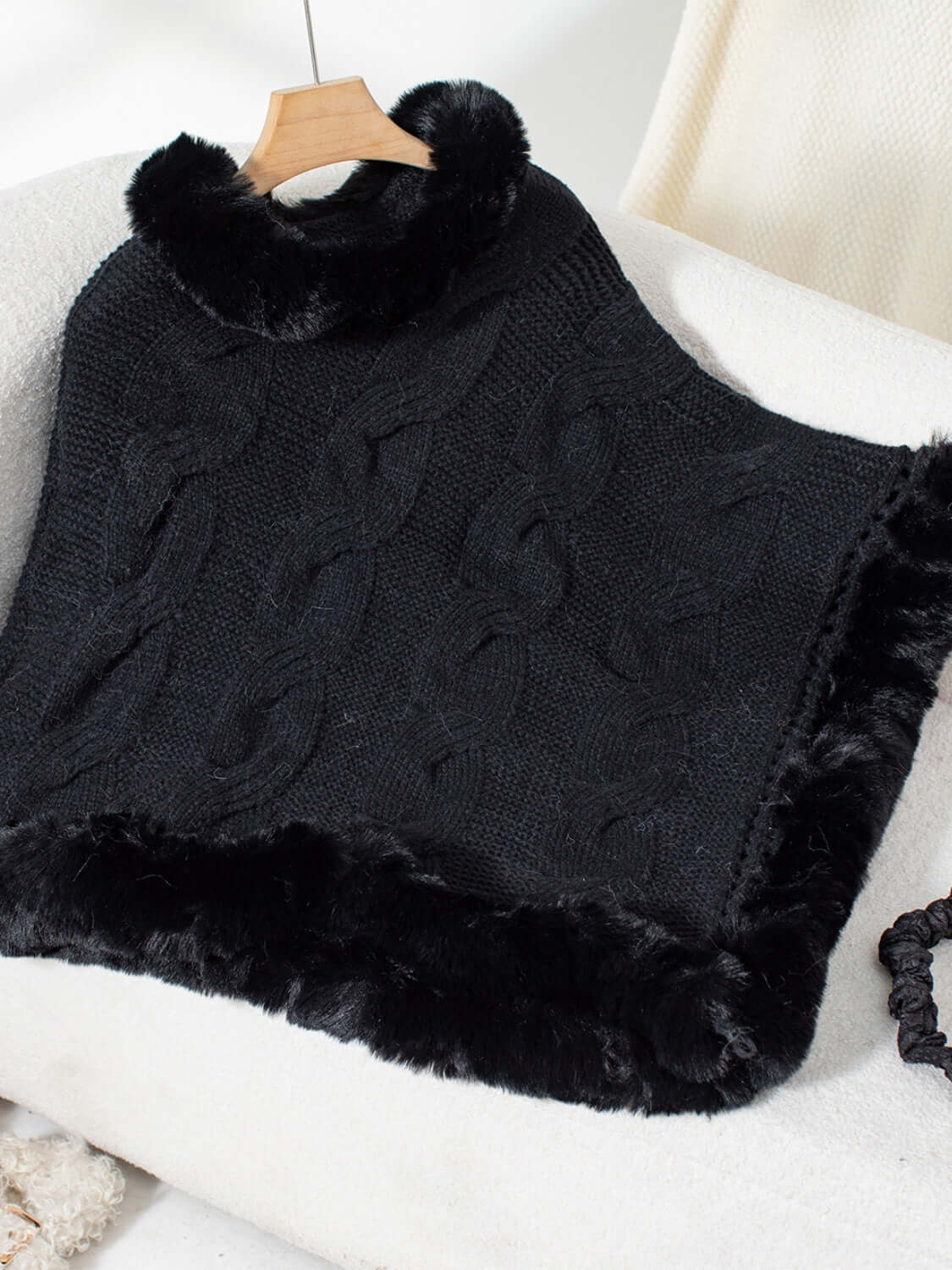 Bella Road black fuzzy hem cable-knit poncho draped over a chair, showcasing cozy winter style and texture.