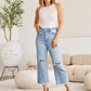 Woman wearing Tummy Control High Waist Raw Hem Distressed Jeans | Petite from RFM Jeans in a stylish living room setting.