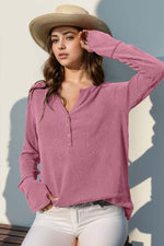 Woman wearing Double Take Full Size Notched Thumbhole Long Sleeve T-Shirt in pink with a hat, standing against a light background.