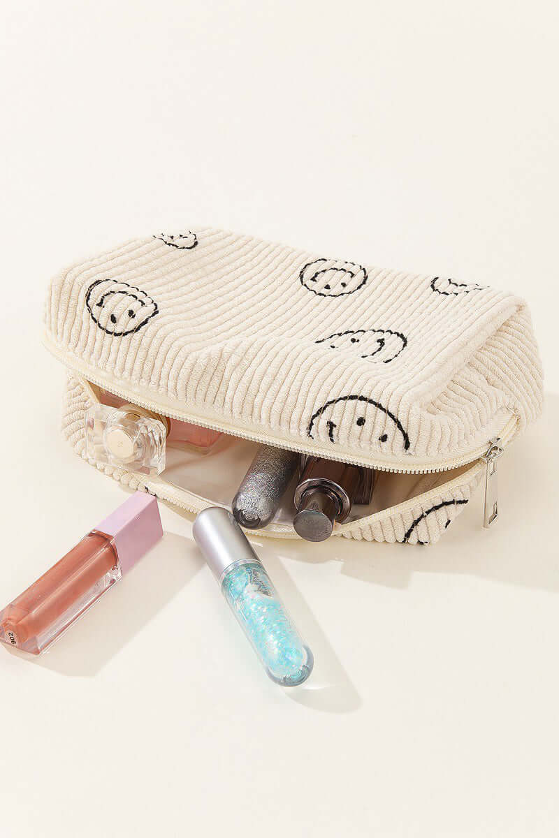 Smiley face corduroy cosmetic pouch with makeup products spilling out, adding a cheerful touch to beauty organization.