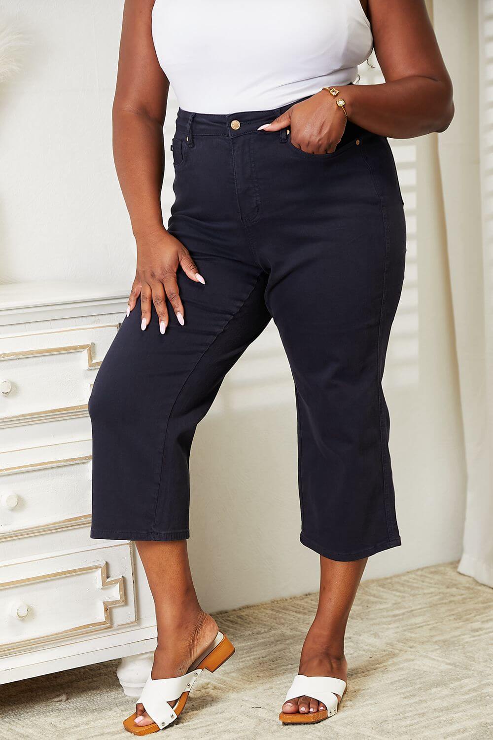 Woman wearing high waist tummy control wide cropped Judy Blue jeans in garment-dyed finish standing indoors.