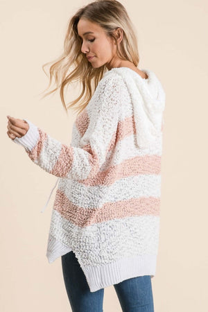 Woman wearing Reborn J high-low striped popcorn hoodie sweater with adjustable drawstrings in cozy, textured knit.