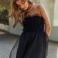 Woman wearing a black mesh ruffle tube top swing dress with a pearl necklace, embodying elegance and style in a summer setting.