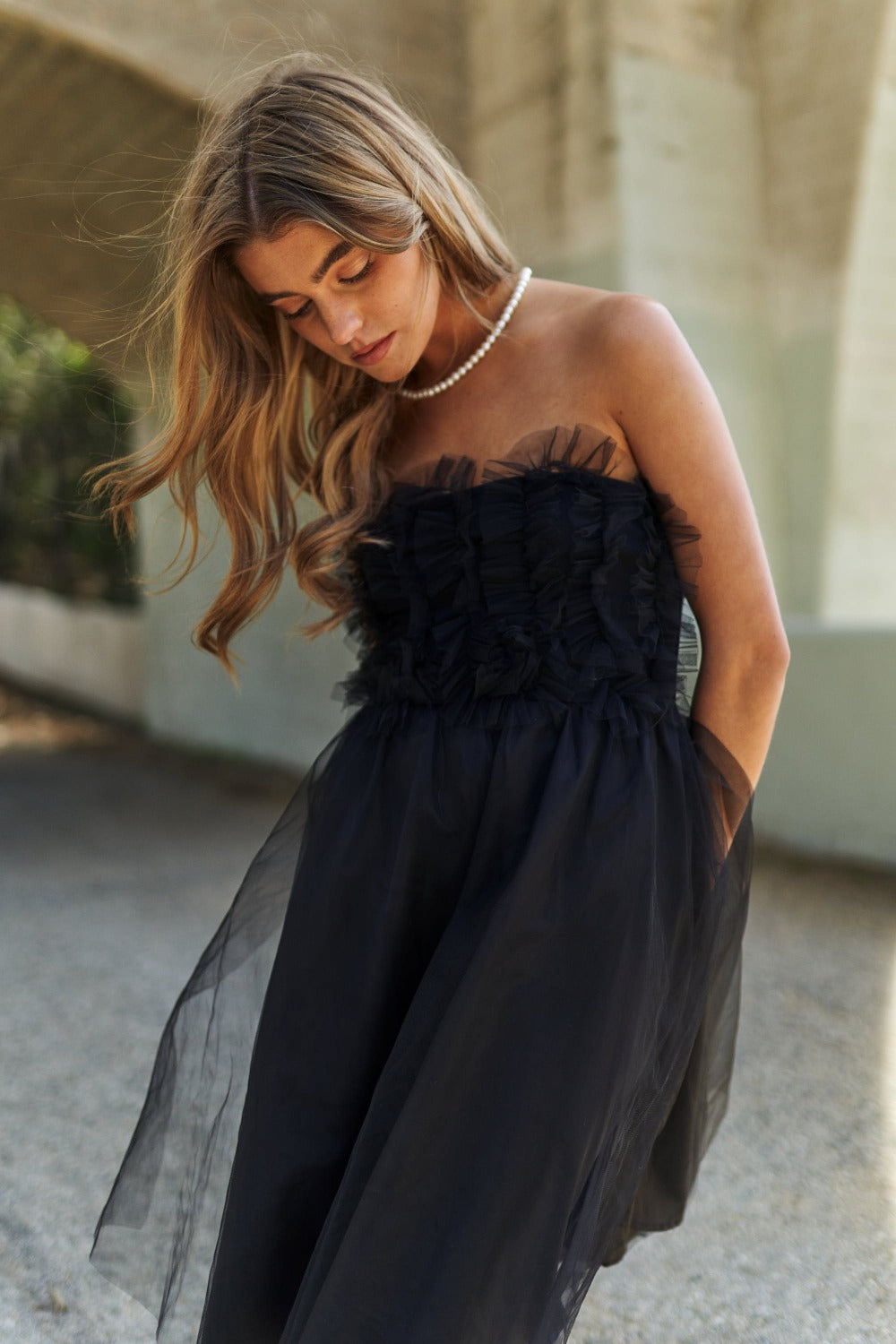 Woman wearing a black mesh ruffle tube top swing dress with a pearl necklace, embodying elegance and style in a summer setting.