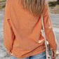 Woman wearing Bella Road Hey Boo Graphic Round Neck Long Sleeve Sweatshirt in orange, styled with light-wash jeans and crossbody bag.