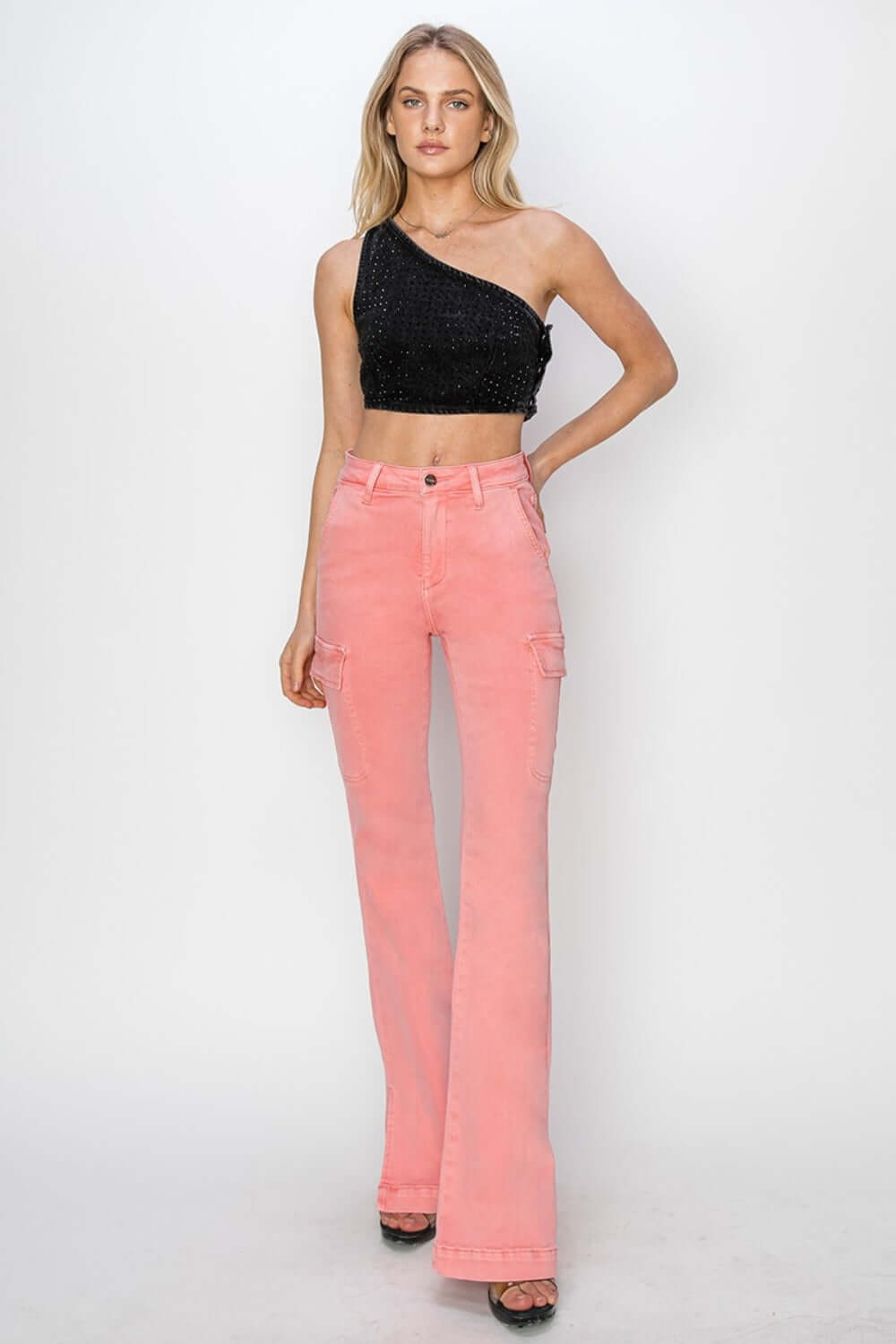 Model wearing high-rise side slit cargo bootcut jeans in pink paired with a one-shoulder black top, showcasing edgy and versatile style by Risen Jeans