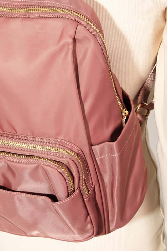 Close-up of a stylish rose pink nylon backpack with multiple zippered pockets and gold accents. Perfect for organization!