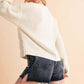 Stylish woman wearing a cozy white cable knit sweater and denim shorts, showcasing a relaxed drop shoulder silhouette.