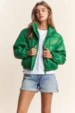 Green faux leather cropped puffer jacket with turtleneck, zipper, and snap closures, perfect for fall and winter fashion.