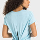 Stylish woman in a light blue Millennia Tie Back Sports Tee showcasing the trendy back tie design. Perfect for workouts!