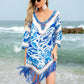 Woman wearing blue and white cutout V-neck three-quarter sleeve cover-up with tassels, standing on a beach.