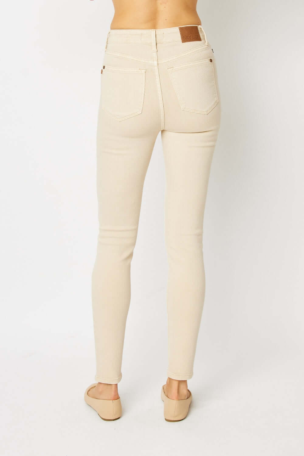 Back view of model wearing Garment Dyed Tummy Control Skinny Jeans by Judy Blue Jeans in beige color, showcasing high-rise waist and fit.