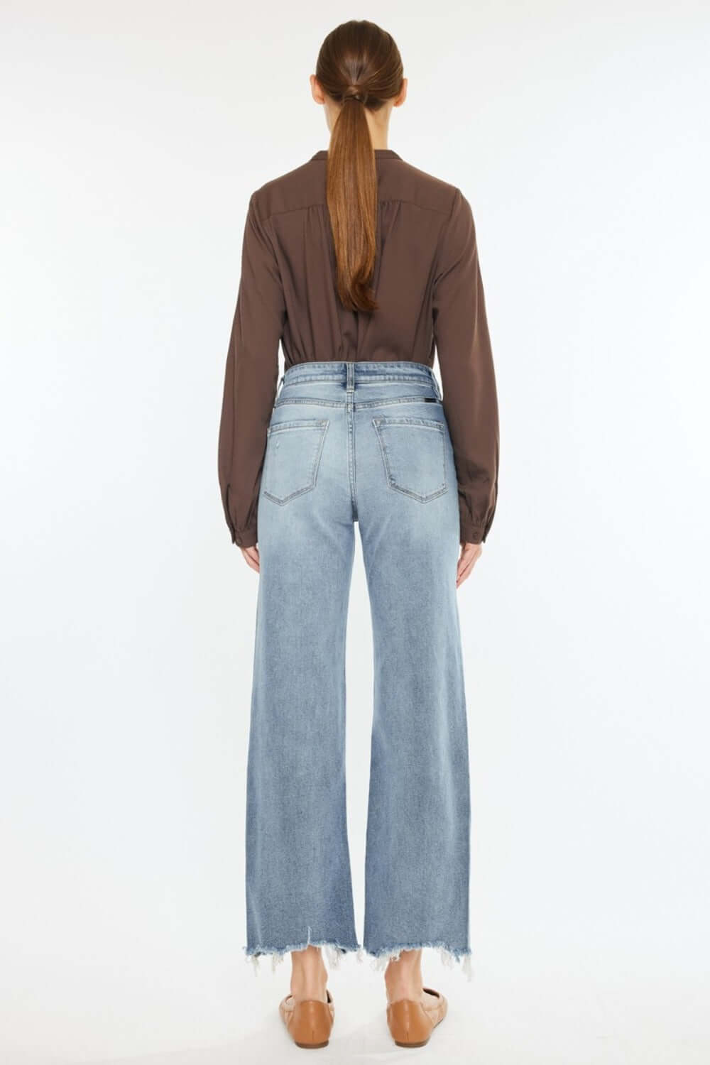 Woman wearing Kancan high-rise slim wide leg jeans in light wash with unique hem details, showcasing a modern fit from the back.