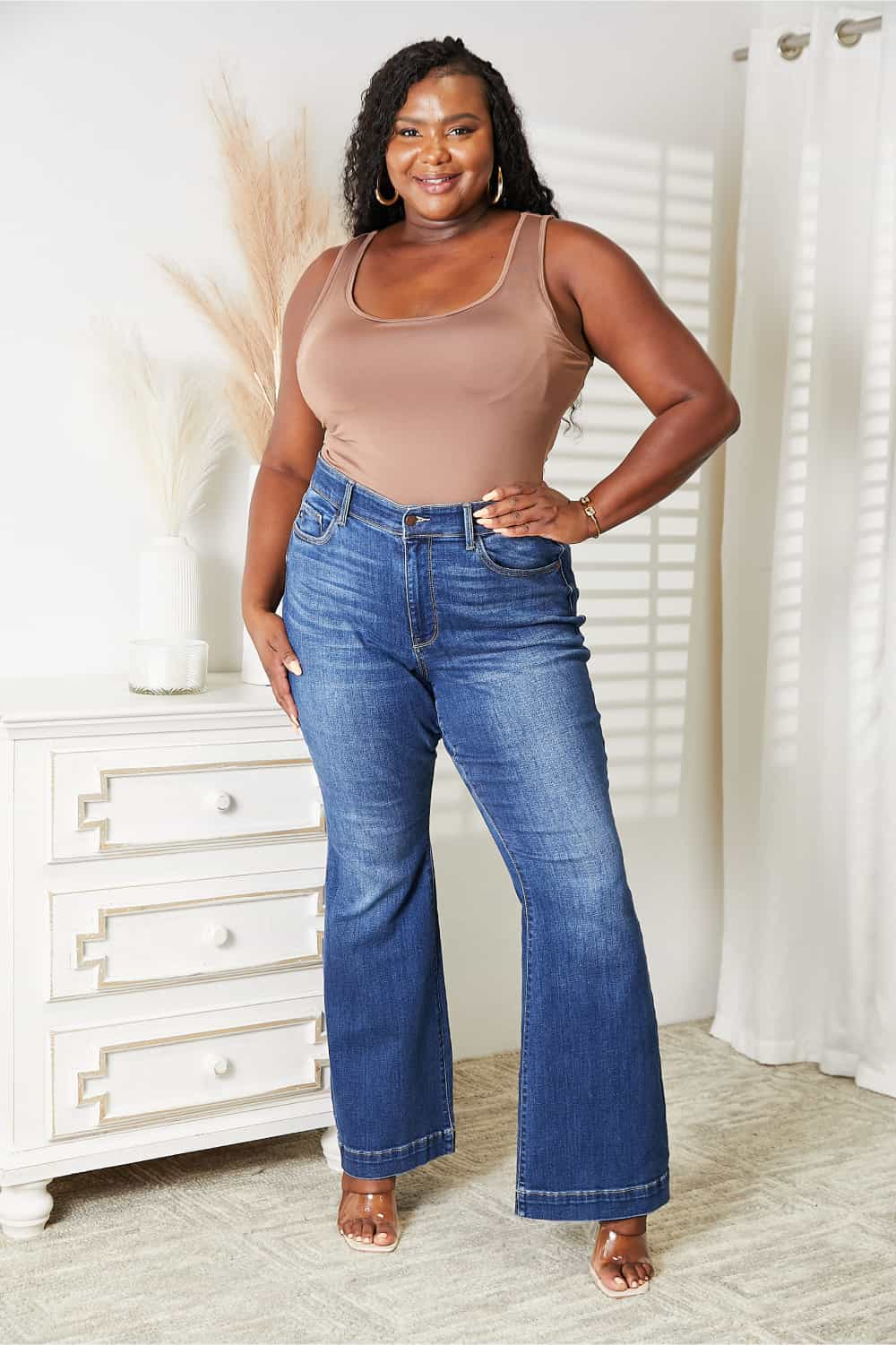 Woman wearing Everyday Full Size Basic Tank Bodysuit in beige paired with high-waisted jeans, standing confidently indoors.