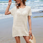 Woman in a stylish openwork cover-up and hat on the beach, showcasing summer fashion by the ocean.