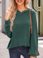 Woman wearing a green textured kangaroo pocket long sleeve hoodie, paired with jeans, outdoors.