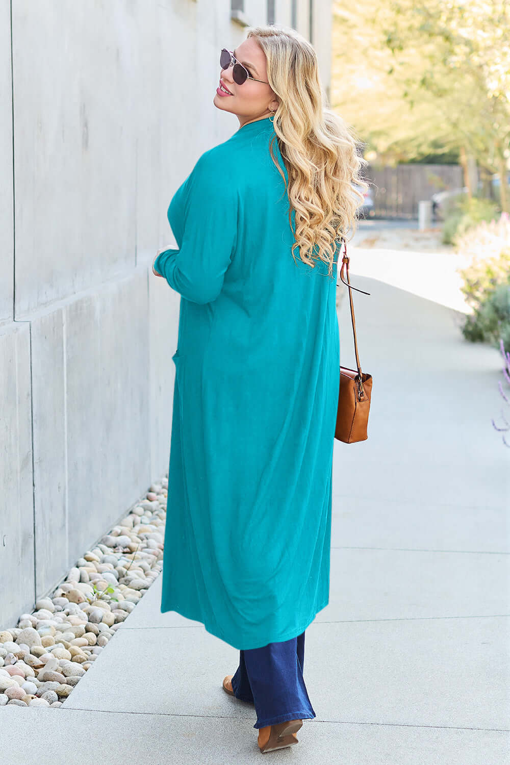 Woman wearing turquoise open front long sleeve cover up with pockets, walking on a sidewalk