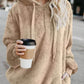 Woman in a cozy beige quarter-zip teddy hoodie holding a coffee cup on a city street.