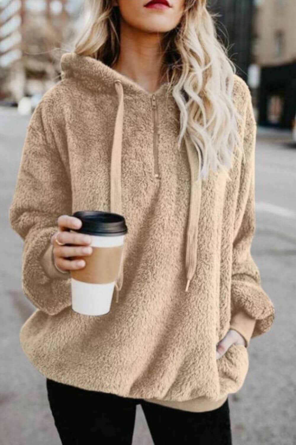 Woman in a cozy beige quarter-zip teddy hoodie holding a coffee cup on a city street.