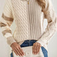 Stylish woman in Bella Road cable-knit color block round neck sweater paired with jeans, holding a chic clutch.