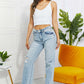 Woman wearing Allie 90's Dad Jean in light wash with distressed details, raw hem, and high waist; paired with a white tank top and heels.