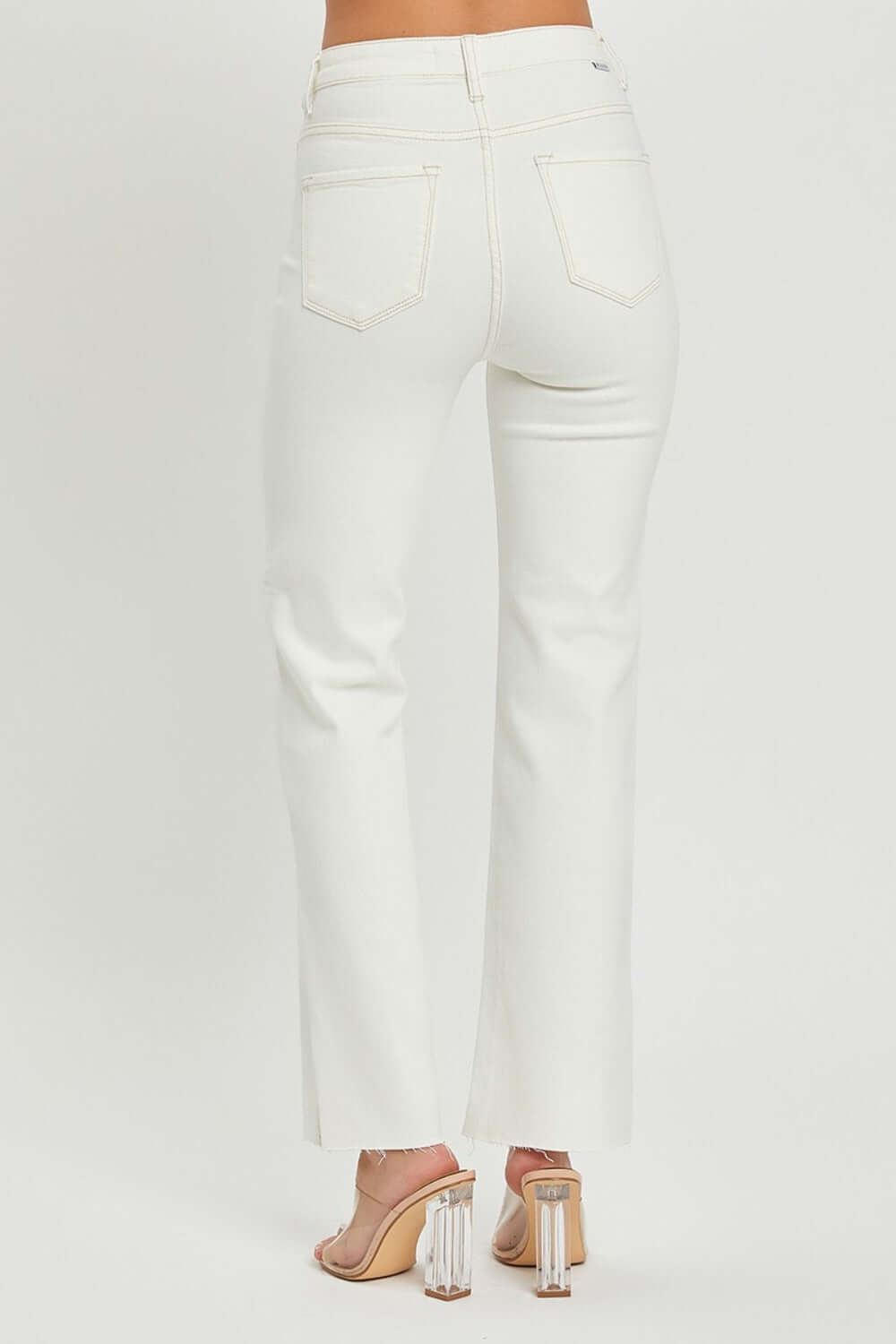 White high-rise straight jeans with raw hem and pocket details, shown from the back, paired with clear block heels.