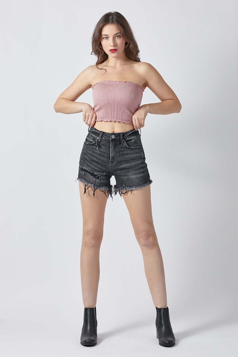 Woman wearing Risen Jeans raw hem denim shorts with pockets, paired with a pink strapless top and black ankle boots.