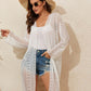 Woman wearing a sheer geometric open front long sleeve cover up with denim shorts, white top, sun hat, and sunglasses.