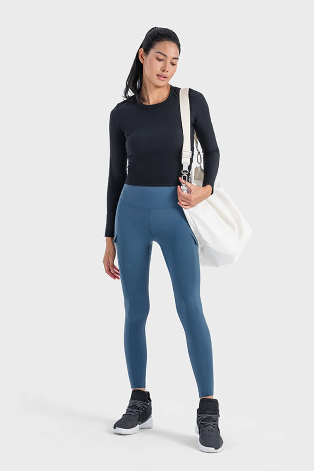 Woman in a black long sleeve sports top and blue leggings, ready for a workout with a stylish gym bag.