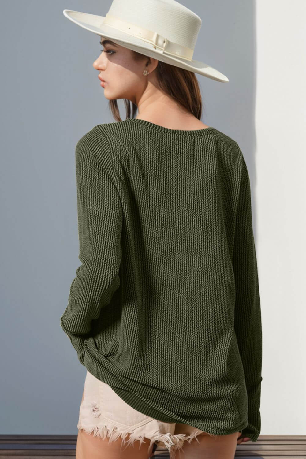 Woman wearing a green knit long sleeve t-shirt and white hat from back view.