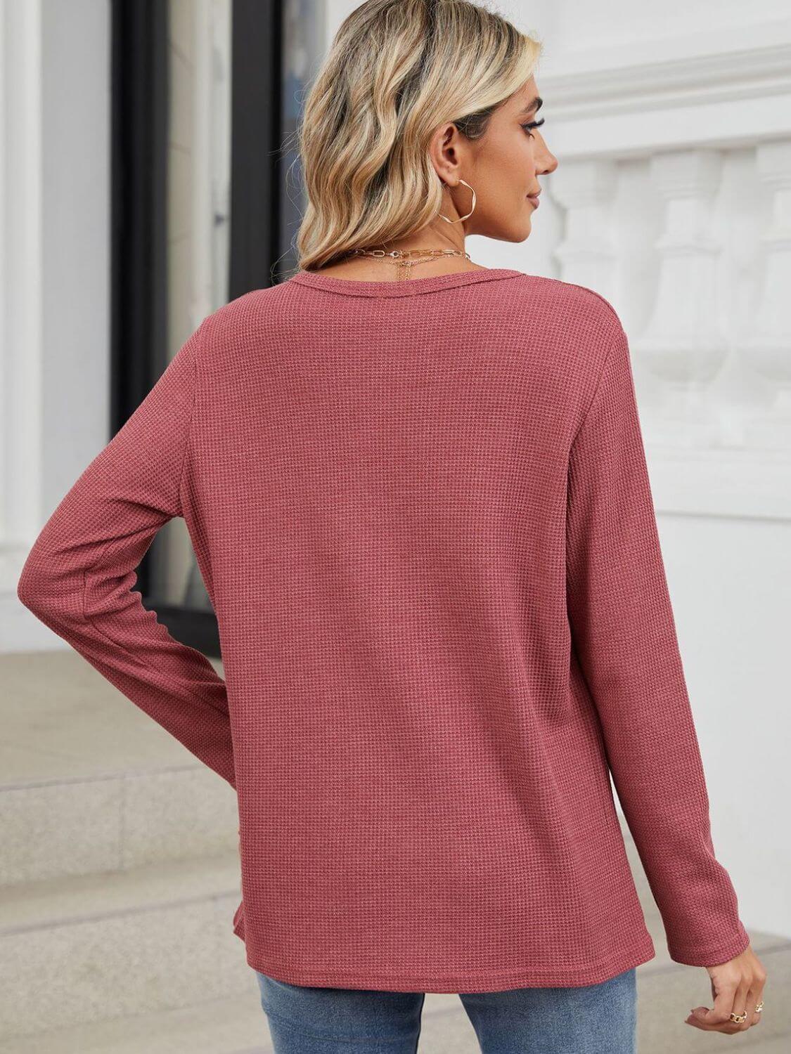 Woman wearing Bella Road waffle-knit notched long sleeve T-shirt in dusty rose, viewed from the back, paired with blue jeans.